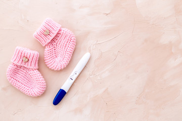 Positive pregnancy test. Baby girl concept with pink booties on beige background top-down copy space