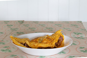 Omelette, a delicious homemade omelet with meat and onion served on a white plate on the table.
