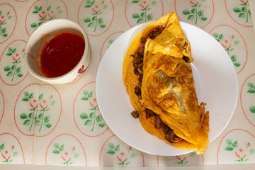 Omelette, a delicious homemade omelet with meat and onion served on a white plate on the table.