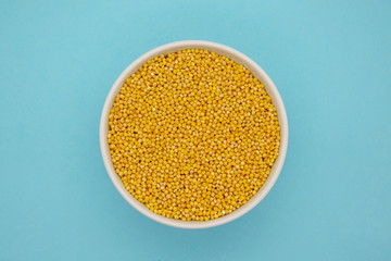 Dry millet in white ceramic bowl isolated on blue. Spilled millet.