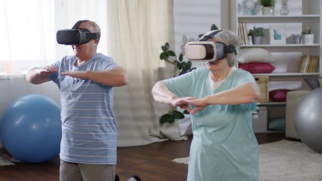 Senior man and woman in VR glasses doing torso rotation exercise in the living room while working out together at home