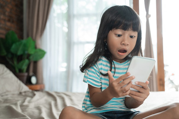 shocked toddler while looking at her mobile phone playing game at home