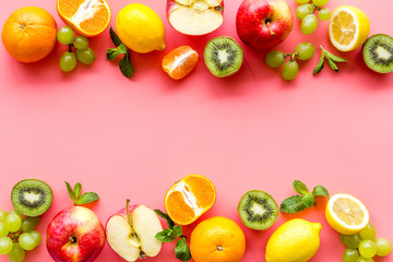 Fresh fruits background with citruses, apple, kiwi and grape on pink table top-down frame copy space