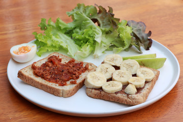 Bread with chili paste and bread with Banana, Half boiled egg and vegetables in the white round plate.