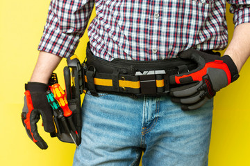 Electrician or professional Builder in the installer's belt with tools on a yellow background. Electrician's tools in black bags on the worker 's belt. Banner with space for text