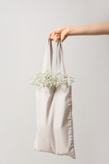 Female hand with flowers in eco bag on light background