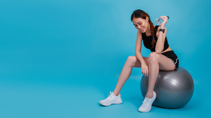 Asian beautiful happy woman wearing smart watch holding water bottle and sitting on fit ball after...