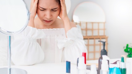 Asian beautiful young businesswoman feeling headache and stress in make-up room background with cosmetic.Concept of Healthcare and Health problems on the face.