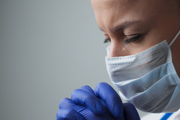 A female doctor therapist in a white robe, mask and gloves. Face close-up. The doctor cries and...