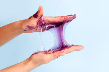 Young girl hands with sticky purple slime on blue background, liqiud wax for depilation, conceptual flyer banner with copy space, antistress relax, modern kids hobby