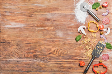 Ingredients for tasty pizza with grater and cutter on wooden background