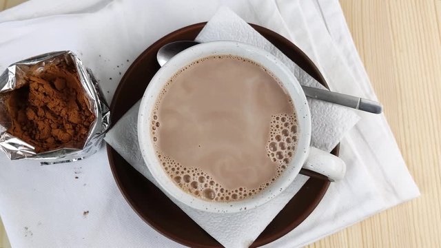 Cocoa drink in cup is moved by streaks. Brown natural ingredient for making hot chocolate. Close-up, wooden table, white napkin, top view