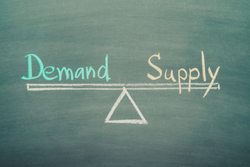 Text word demand and supply balance on seesaw drawing writing on chalkboard or blackboard background. Demand and supply in business marketing, investment concept. Real photo, not illustration.