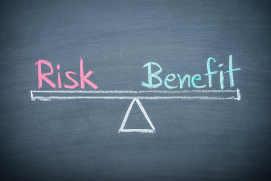 Text word risk and benefit balance on seesaw drawing writing on chalkboard or blackboard background. Concept of risk and benefit analysis in business, financial and investment.