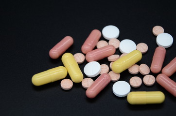 white and pink tablets and pink and yellow capsules on a black background. Coronavirus Covid-19. Copyspace. world pharmaceutical day