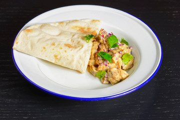 Meat with gravy and fresh greenery served with a piece of lavahs bread on white plate over dark rustic background.
