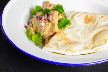 Meat with gravy and fresh greenery served with a piece of lavahs bread on white plate over dark rustic background.
