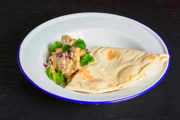 Meat with gravy and fresh greenery served with a piece of lavahs bread on white plate over dark rustic background.