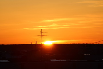 Sun over the horizon and television antenna in the background clouds in the orange sky at sunset or dawn backlit by the sun. Place for text and design.