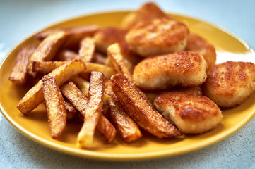 Tasty homemade potato french fries with chiken nuggets on yellow dish