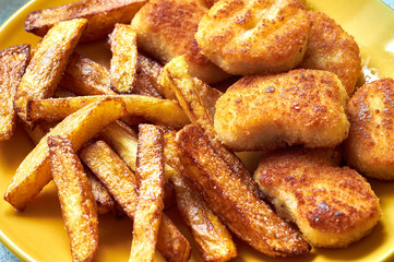 Tasty homemade potato french fries with chiken nuggets on yellow dish