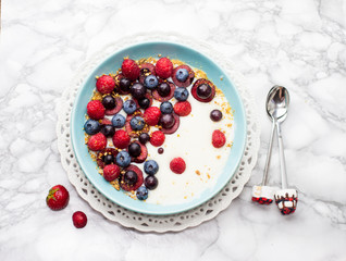 Blue bowl of hot oatmeal breakfast cereal with fresh berries, strawberries, cherries and blueberries from above.