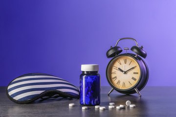 Alarm clock, sleep mask and pills on table