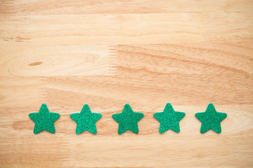 Green glitter five stars shape put on wooden table background. Services rating customer experience, satisfaction, and feedback score concept. Customer evaluation for product or service improvement.