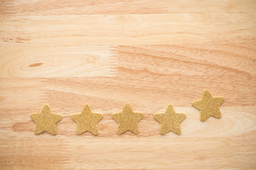 Golden glitter five stars shape put on wooden table background. Services rating customer experience, satisfaction, and feedback score concept. Customer evaluation for product or service improvement.