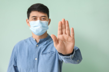 Asian man in mask showing STOP gesture on color background. Concept of coronavirus epidemic