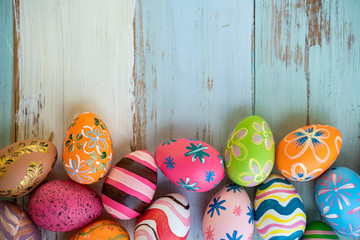 flat lay of colorful vibrant red green pink and orange easter eggs with stripe and flower pattern painted on, laying on side of blue wooden table background representing celebration easter holidays