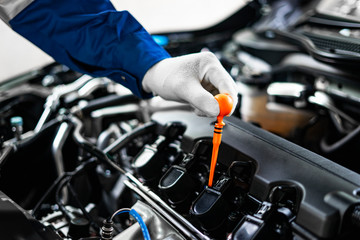 concept of male asian car mechanic holding siphon tube oiling on the car engine, for repair and maintenance services, wearing a white glove and blue garment overalls with front car engine interiors