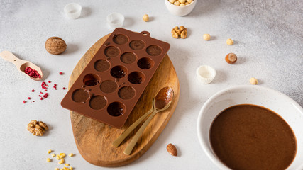 Making chocolate candies in mold and bowl with melted chocolate on light background. Homemade candies. Side view