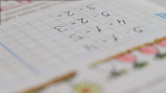 Preschool boy toddler, holding pencil, writing or doing math homework at the table. Hands close up