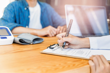 Fototapeta premium close up of asian female doctor witting on a documentation on a clipboard on diagnosing patient health or filling in a medical verification form of the patient, sitting in hospital office medical room