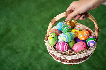 close up iof asian girl holding a basket decorate as bird nest with straw hay colorful easter eggs with flower, stripes patterns of red blue green oranges vibrant colors, in isolated grass background