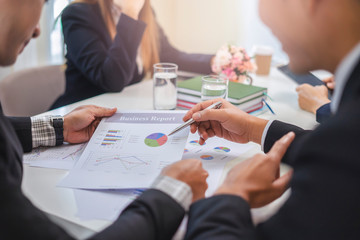 businesswoman and businessman working together in a group in an office, all pointing on the paper together in teamwork conversing and planning strategy using data and statistics of charts and graphs
