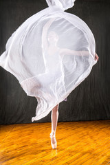 Young woman ballerina dancing with white fabric in the studio.