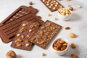 Milk chocolate bars with nuts on light background with molds. Homemade organic chocolate. Handmade tasty presents. Side view