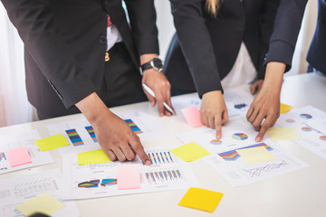 businesswoman and businessman working together in a group in an office, all pointing on the paper together in teamwork conversing and planning strategy using data and statistics of charts and graphs