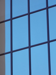 The outer window of the facade of a building, which reflects a cloudless sky.