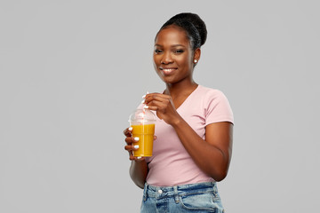 people and drinks concept - happy african american young woman drinking takeaway orange juice from...