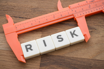 Measuring word RISK with vernier caliper tool on wooden table background. Planning, risk management...