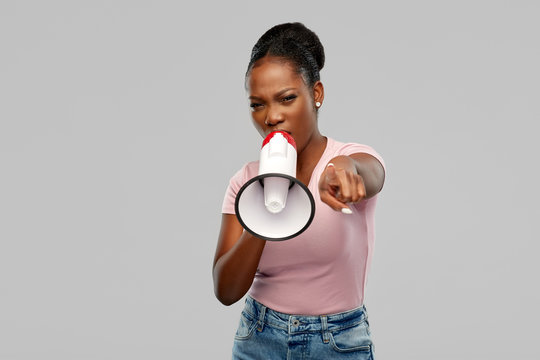 communication, feminism and human rights concept - angry african american young woman speaking to megaphone over grey background