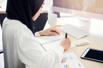 multiethnic asian female muslim working in office as team writing notebook of statistics to strategize and planning work concept of diversity of culture different race type people co-working together