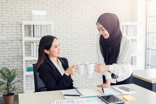 multiethnic asian female muslim working in office as team having break time from work drinking cups of tea and coffee, concept of diversity of different culture race type of people co-working together