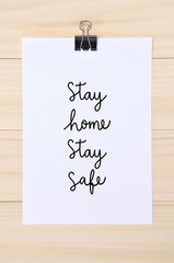 Stay home stay safe hand lettering on white paper with wooden background