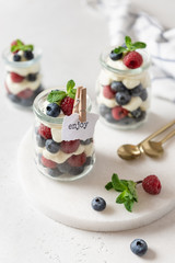 Sweet homemade dessert parfait or trifle with raspberries and blueberries served in glass jars. Summer dessert, confectionery menu.