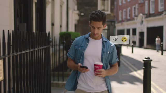 Handsome young man walking the city chatting on social media using happy emoticons. Attractive guy using a smartphone with emoji that mean love, friendship.