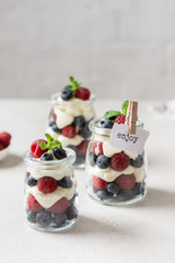 Fresh berry trifle. Raspberry and blueberry parfait with cheese cream and mint served in glass jars on white background. Summer dessert. Confectionery menu